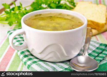 Green pea soup in a white bowl on a green napkin, bread, spoon, parsley on a background of a linen napkin