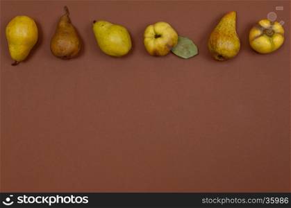 Green pears and quince in row on brown background with copy space