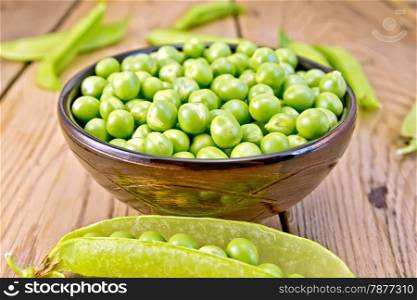Green peas in a brown bowl, pea pods on a wooden board