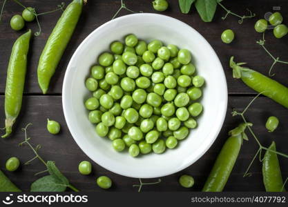 Green peas in bowl on wooden table background. Top view