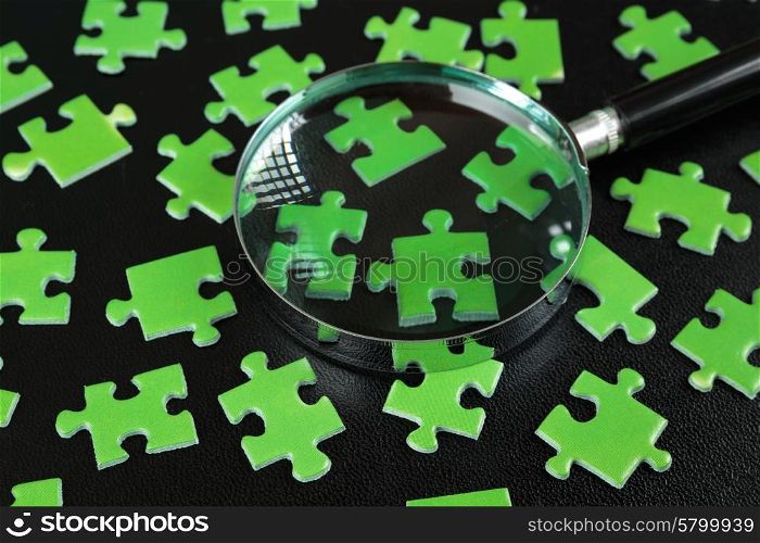 Green puzzles and magnifying glass on a black leather background