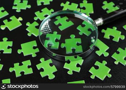 Green puzzles and magnifying glass on a black leather background