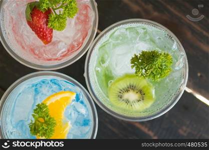 Green Red Blue Italian Soda Cold Beverage and Kiwi Strawberry Lemon Fruit and Parsley. Green Red Blue Italian Soda Cold Beverage on wood table for food and drink category
