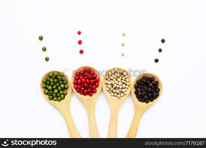 Green, red white and black peppercorns with wooden spoon on white background.