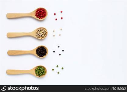 Green, red, white and black peppercorns with wooden spoon on white background. Copy space