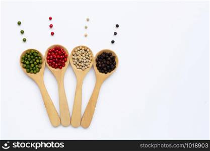 Green, red, white and black peppercorns with wooden spoon on white background. Copy space