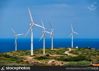 Green renewable alternative energy concept - wind generator turbines generating electricity. Wind farm on Crete island, Greece with small white church. Wind generator turbines. Crete island, Greece