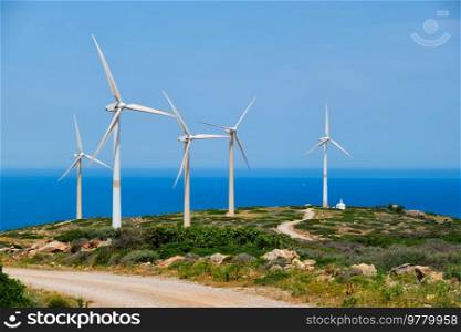 Green renewable alternative energy concept - wind generator turbines generating electricity. Wind farm on Crete island, Greece with small white church. Wind generator turbines. Crete island, Greece