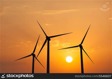 Green renewable energy concept - wind generator turbines in sky on sunset