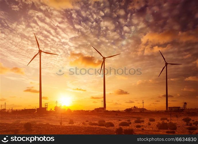 Green renewable energy concept - wind generator turbines sihouettes on sunset. With lens flare and light leak. Wind generator turbines sihouettes on sunset