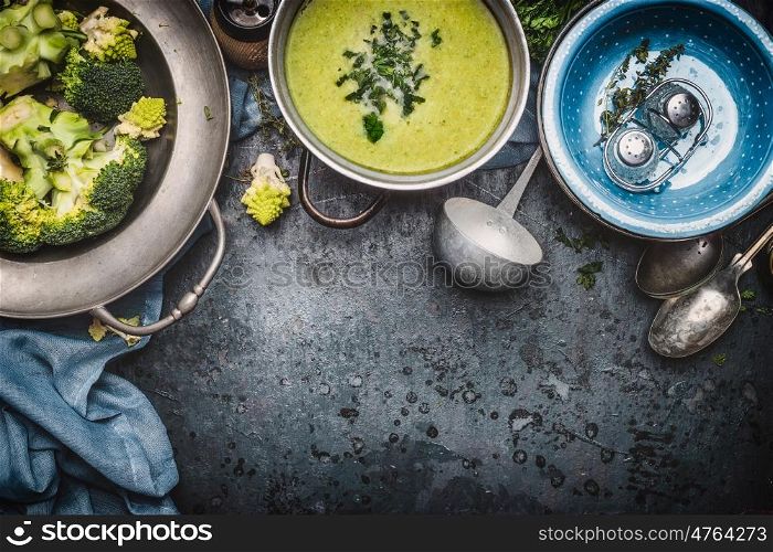 Green Romanesco and broccoli soup with cooking ingredients, ladle , bowls and spoons on dark rustic background, top view, border. Healthy and vegetarian food or diet nutrition concept.