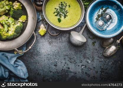 Green Romanesco and broccoli soup with cooking ingredients, ladle , bowls and spoons on dark rustic background, top view, border. Healthy and vegetarian food or diet nutrition concept.