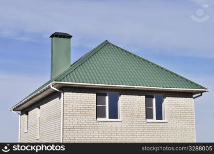 Green roof of new white brick house on blue sky background