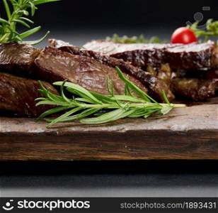 green rosemary branch on a background of fried beef slices on a brown wooden board