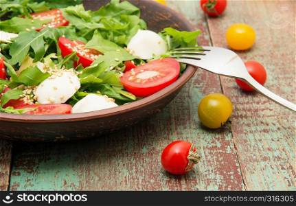 Green salad made with arugula, tomatoes, cheese mozzarella balls and sesame on plate