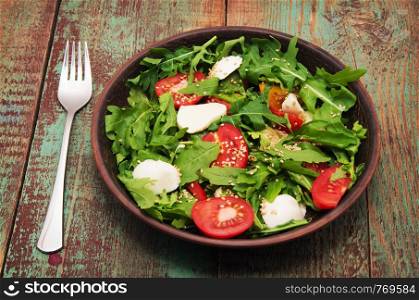 Green salad made with arugula, tomatoes, cheese mozzarella balls and sesame on plate