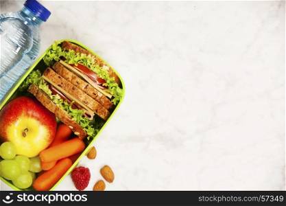 Green school lunch box with sandwich, apple, grape, carrot and bottle of water close up on white wooden background. Healthy eating habits concept. Flat lay composition (from above, top view).