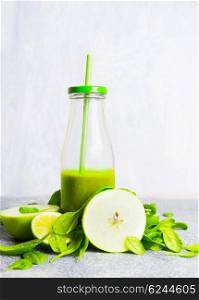 Green smoothie bottle with straw and green ingredients on light wooden background, side view. Healthy lifestyle and detox or diet food concept