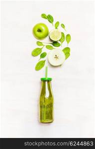 Green smoothie drink in bottle with straw and ingredients ( spinach,apple, lime ) on white wooden background, top view
