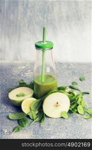 Green smoothie in bottle and ingredients: apple and spinach, on rustic background, front view, retro toned. Healthy, diet or detox beverage concept
