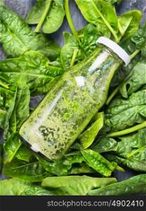Green smoothie in bottle lies on fresh spinach background, top view