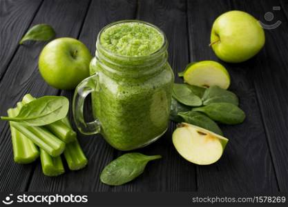Green smoothies with spinach, apple and celery on the black wooden background