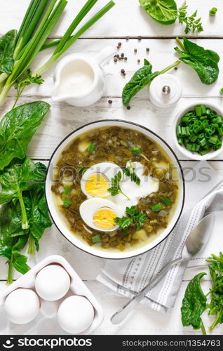 Green sorrel and spinach soup with boiled egg and sour cream on white wooden rustic table, top view
