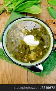Green soup of sorrel and spinach in a bowl with sour cream, quail eggs, bread, spoon on a wooden boards background