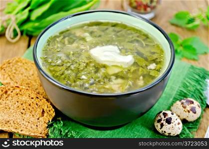 Green soup of sorrel, nettle and spinach in a bowl, quail eggs, bread, pepper against a wooden board