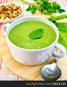 Green soup puree in a bowl with green leaf spinach, spoon on the board, crunches on fabric background