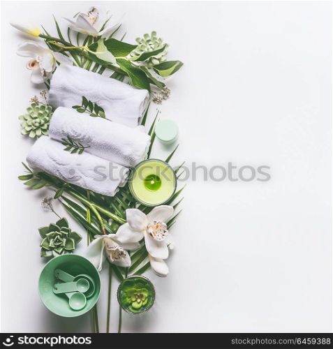 Green spa or wellness background with towels, candle, tropical leaves , orchid flowers, succulents and body and face care tools and accessories on white desktop, top view with copy space.