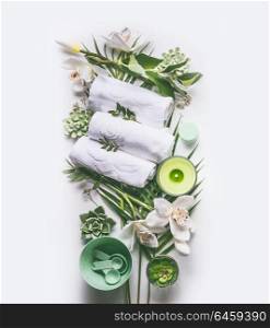 Green spa or wellness composing with towels, candle, tropical leaves , orchid flowers, succulents and body and face care tools and accessories on white background, top view