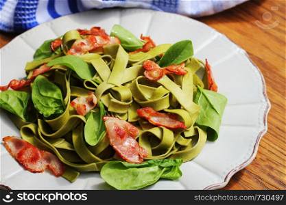 Green spinach pasta with chrispy bacon on wooden table. Gourmet italian meal .. Green spinach pasta with chrispy bacon on wooden table. Gourmet italian meal