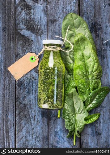 Green spinach smoothie bottle with sign lies on blue wooden background, top view