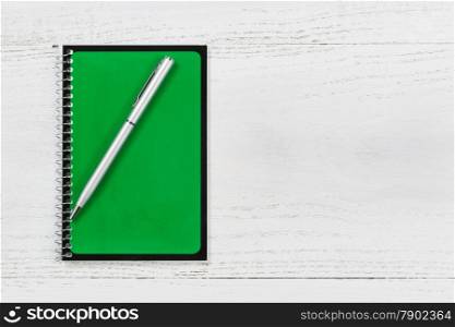 Green spiral notepad with pen on desktop.