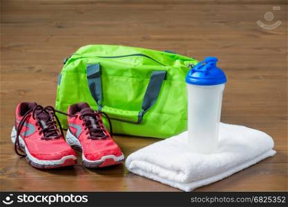 Green sports bag and pink sneakers near a towel with a bottle for fitness