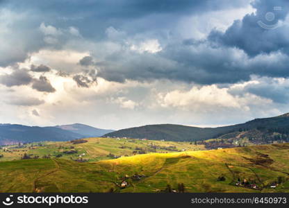 Green spring alpine scene. Mountain village on hillsides. Spring stormy rainy weather