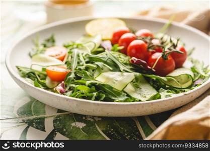 Green spring salad with arugula, cucumbers and tomatoes on tile background. Healthy vegetable vegan dish.. Green spring salad