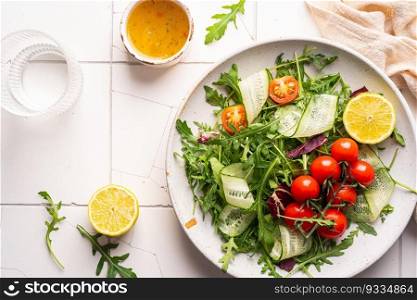 Green spring salad with arugula, cucumbers and tomatoes on tile background. Healthy vegetable vegan dish. Top view. Green spring salad