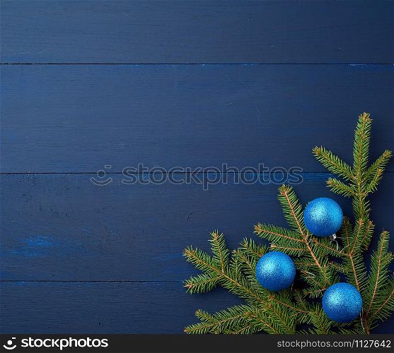 green spruce branches and dark blue shiny Christmas balls on a blue wooden background from boards, festive backdrop for Christmas and New Year, place for an inscription