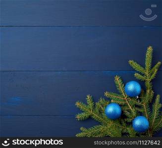 green spruce branches and dark blue shiny Christmas balls on a blue wooden background from boards, festive backdrop for Christmas and New Year, place for an inscription