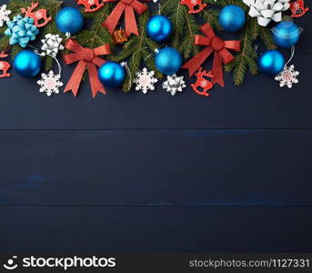 green spruce branches, Christmas blue and pink balls, red shiny bows and carved wooden decor on a blue wooden background from boards