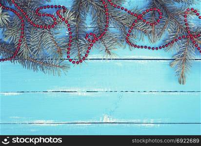 green spruce branches with a red Christmas garland on a blue wooden background of parallel boards, empty space at the bottom