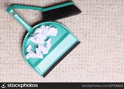 Green sweeping brush and dustpan for house work with garbage papers on floor indoors. Cleaning