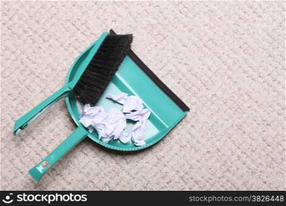 Green sweeping brush and dustpan for house work with garbage papers on floor indoors. Cleaning