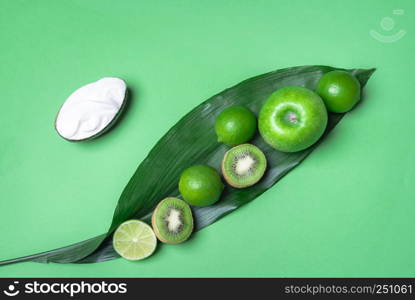 Green tabletop with a big leaf with green fruits on it, apple, kiwi and lime, and fresh yogurt on an avocado shell. Detox concept. Vegetarian food.