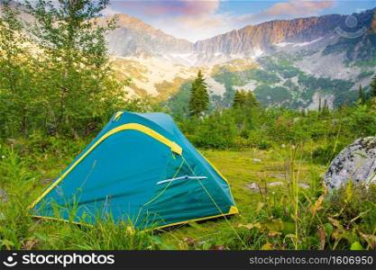 Green tent in forest at foot of mountain range. Hiking to rocks in  valley.