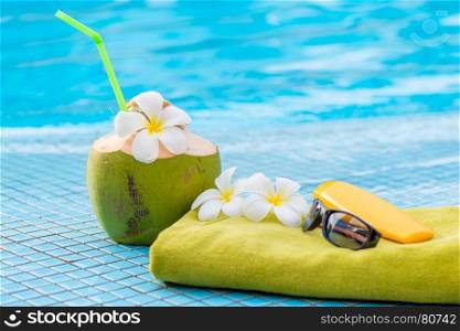 green towel and beach accessories near to a juicy coconut decorated with flowers on the edge of the pool