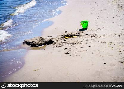 Green toy bucket left by a kid on the sandy beach. Somebody was playing in sand next to sea.. Green toy bucket on beach