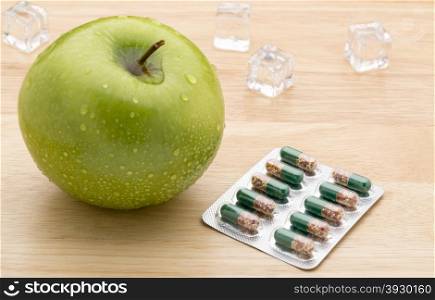 Green transparent pills capsules and fresh green apple. Green transparent pills capsules and fresh green apple on wooden background